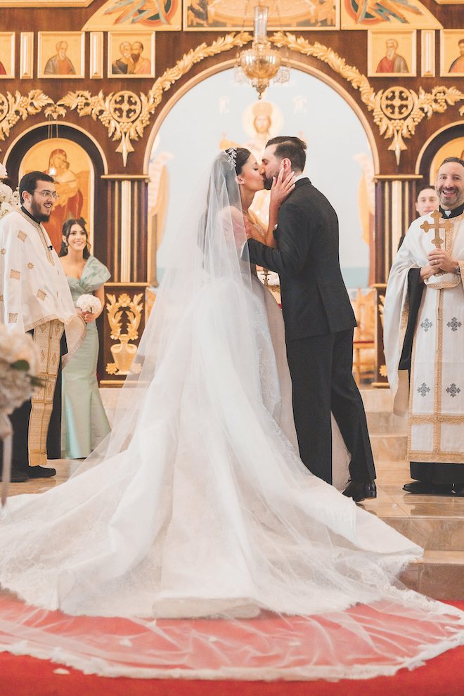 Bride and groom kissing at the beautiful gold detailed altar at the church.