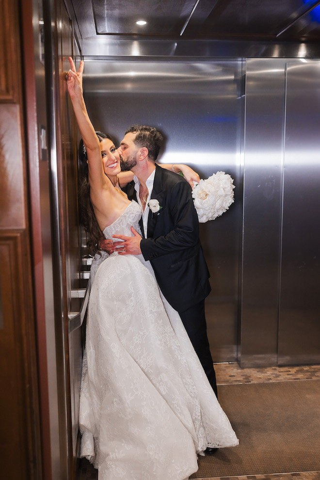 Groom kissing the bride's cheek inside elevator.