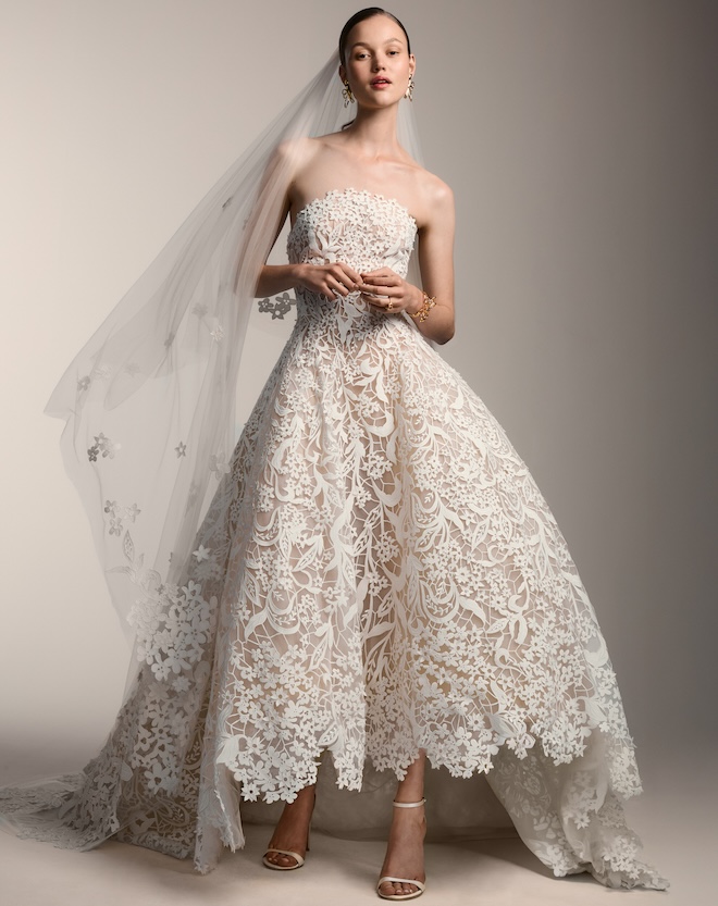 The model wears an Oscar de la Renta gown with lace detailing. 