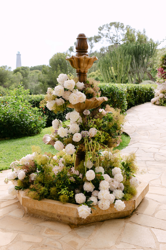 Vintage gold water fountain covered in greenery and white florals for French Riviera destination wedding.