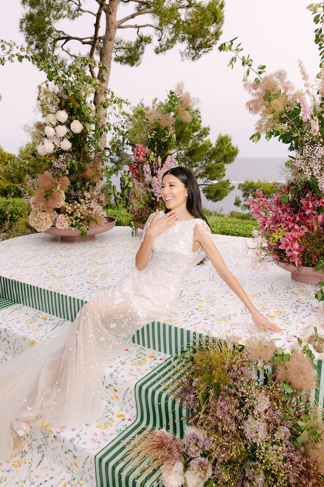 Bride sitting on stairs leading to altar showing her ring surrounded by colorful plants and florals.