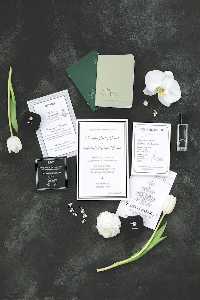 White invitations with black and green details with the rings and white florals around it.