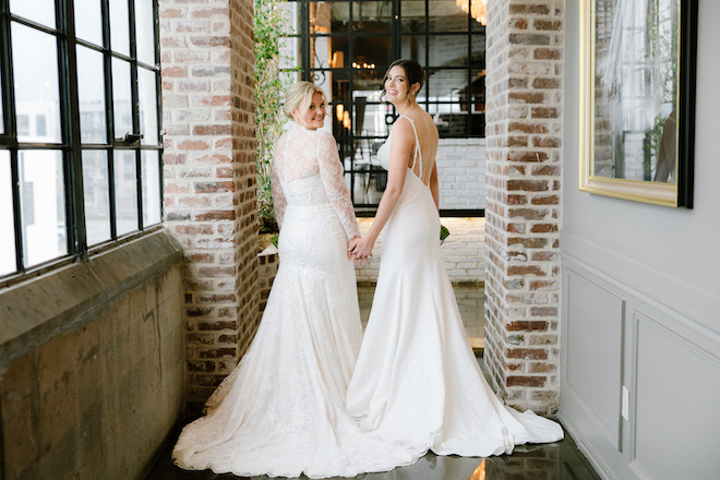 The brides holding hands and looking back before their ceremony in between brick details at The Astorian.