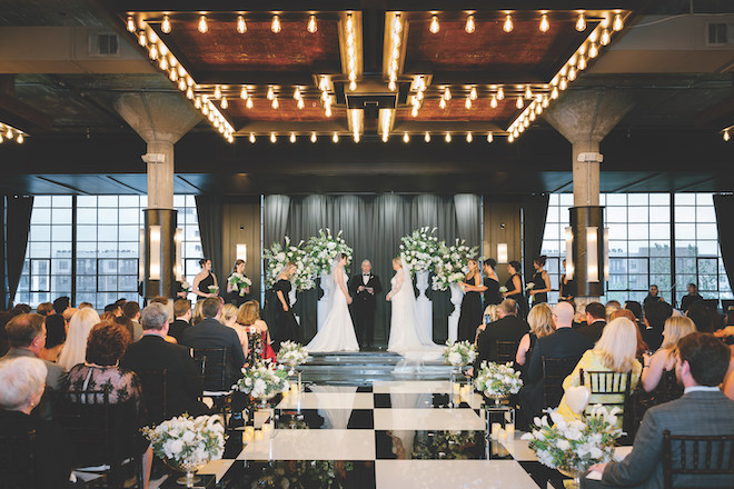 The brides standing at the altar with black and white checkered floor leading to it for chic spring wedding with white blooms.