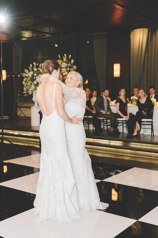 Newlyweds sharing their first dance on black and white checkered dance floor for spring wedding with white blooms.