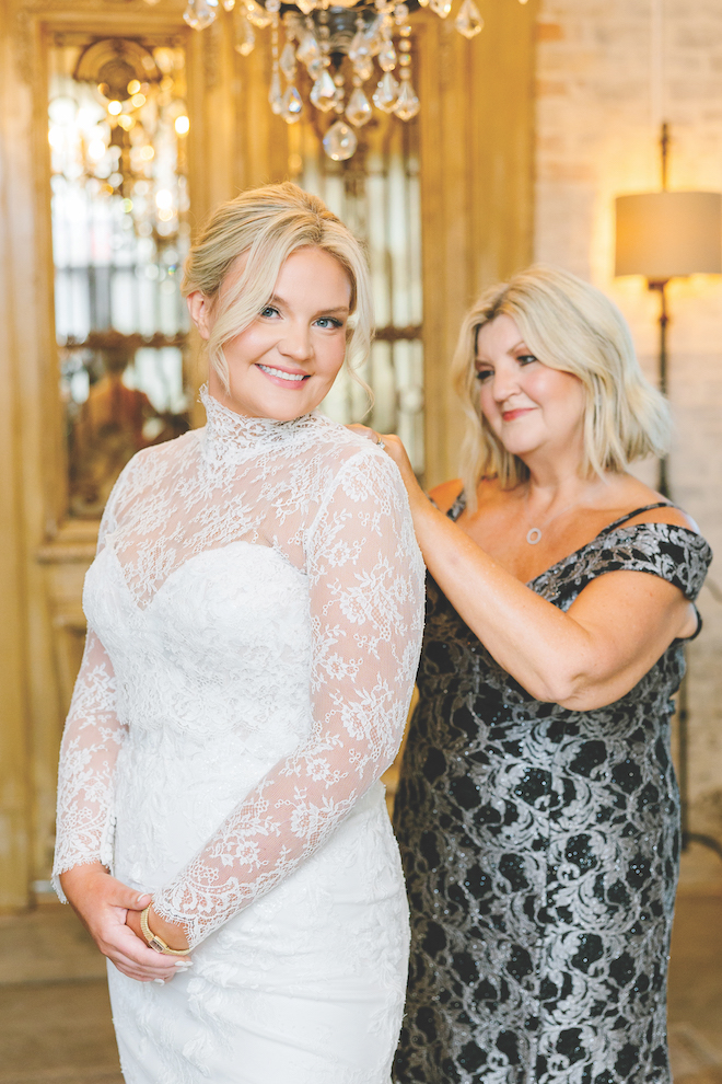 Mother of one of the brides helping her in her long sleeved lace gown before the private vows and ceremony.
