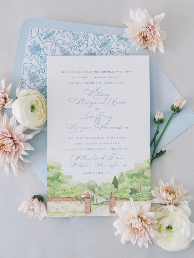 Blue writing on white wedding invitation with a watercolor painting of a park with light pink and white florals.