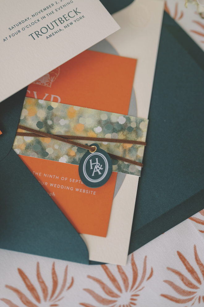 Green, beige, and orange invitations tied with brown suede with an H&A tag on it.