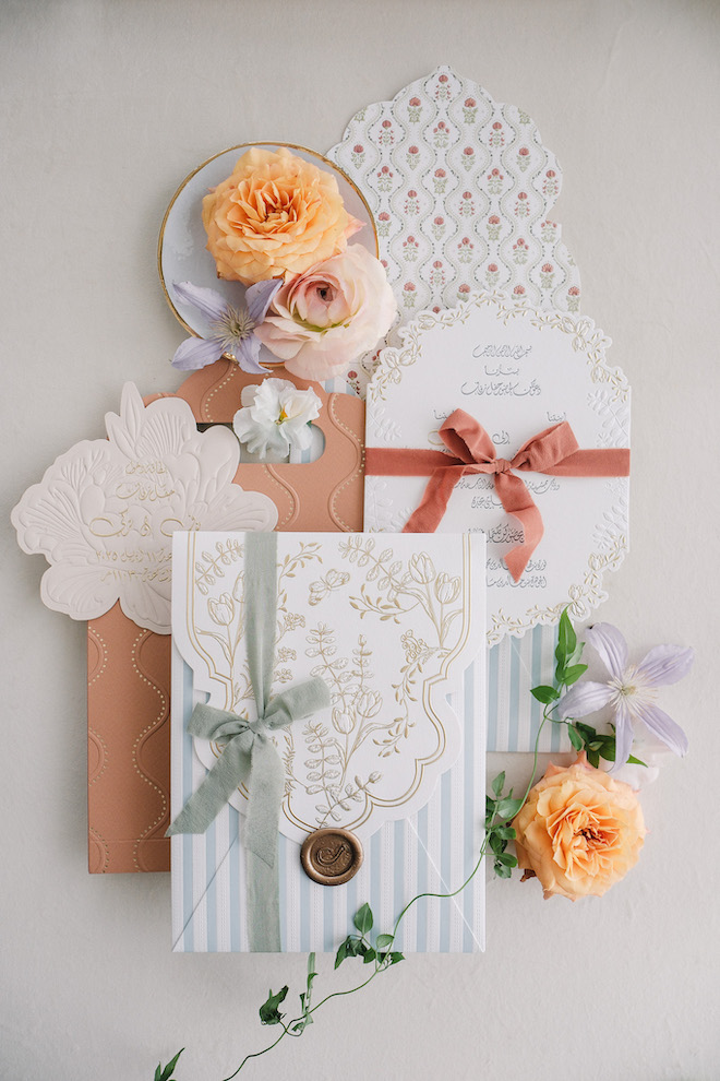 Wedding invitations with blue, white, orange, and purple details with colorful flowers around them.