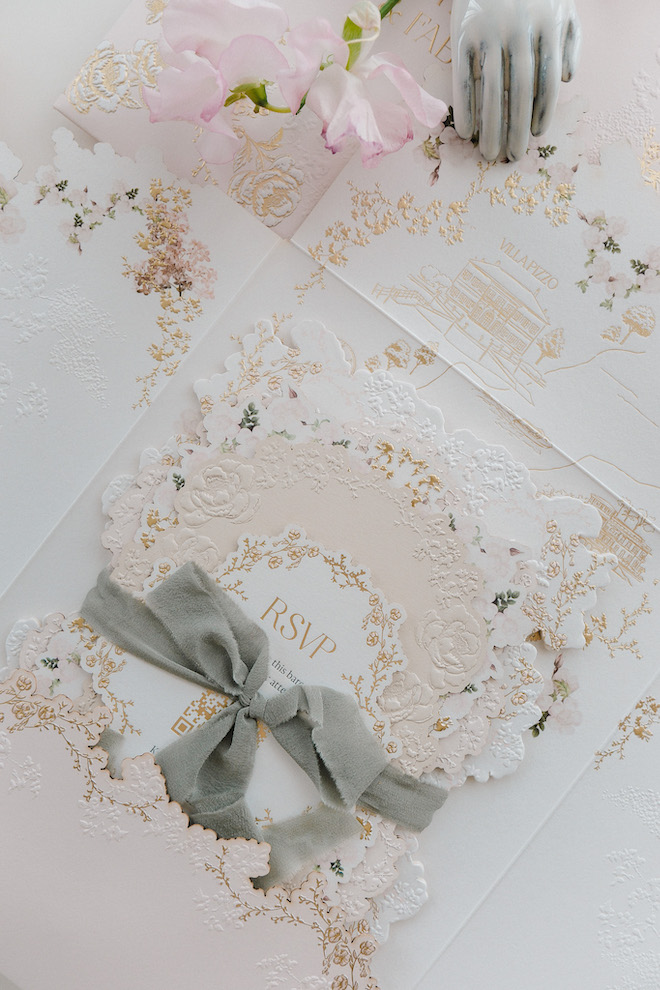 Textured and detailed invitations with gray ribbon with gold and light pink hues.