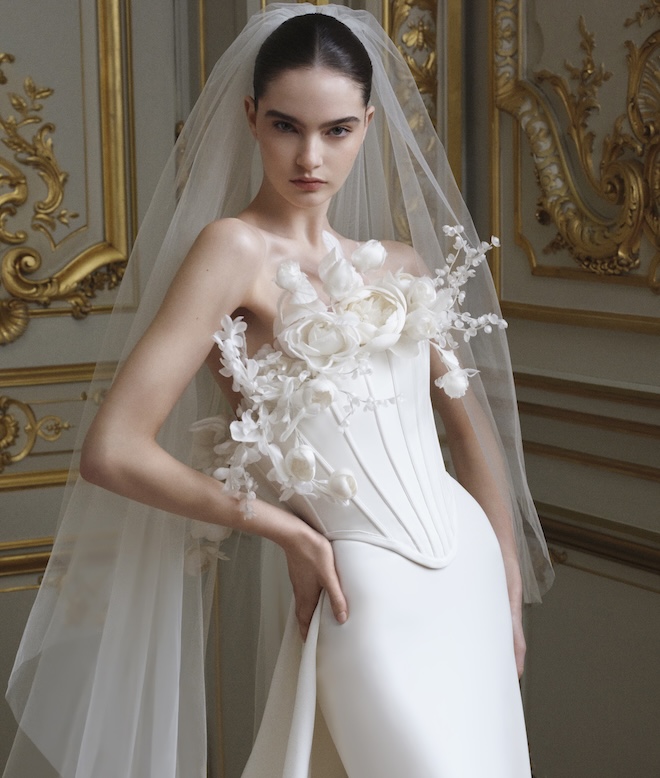 The model wears a corset top with sculptural florals coming out from the top of the dress. 