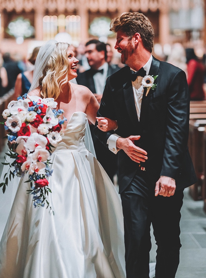 The newlyweds walking down the aisle with locked arms smiling at each other.