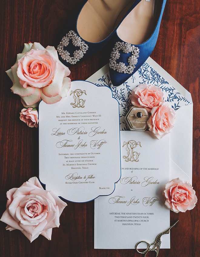 Stationery on hard wood floors with gold and blue details with light pink roses surrounding. 