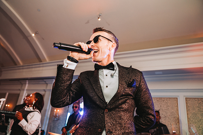 Houston wedding band lead singer performs on stage at the reception with sunglasses.