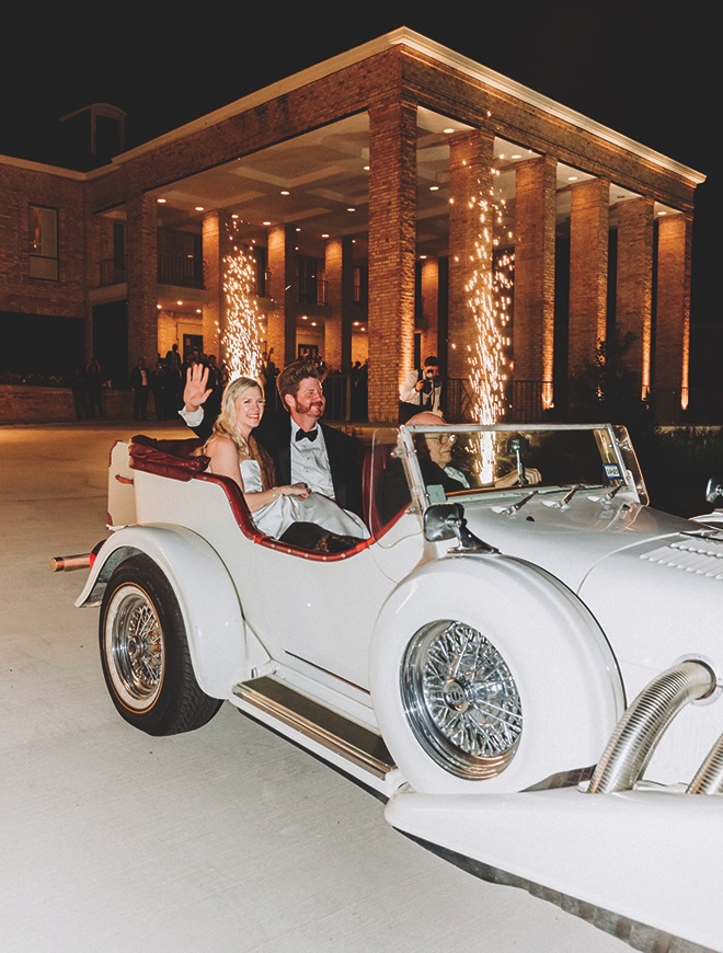 Newlyweds in white vintage getaway car with sparklers lighting behind them.