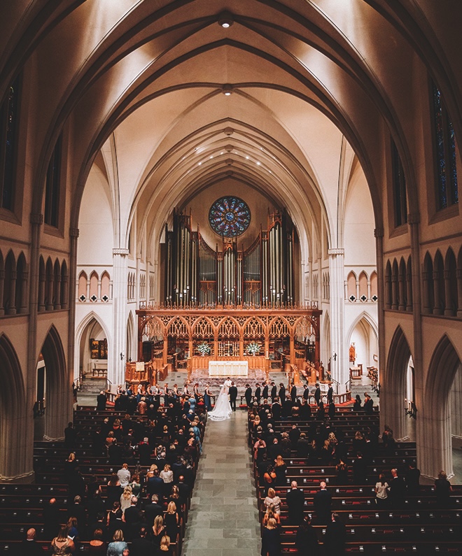 Stunning picture of the inside of the whole church from up high showing bride and groom at the altar and guests behind them in pews.