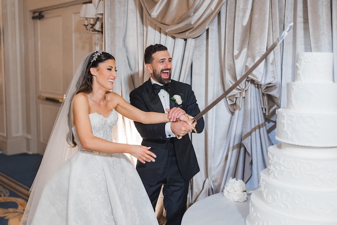 The bride and groom cute into their wedding cake with a ceremonial sword. 