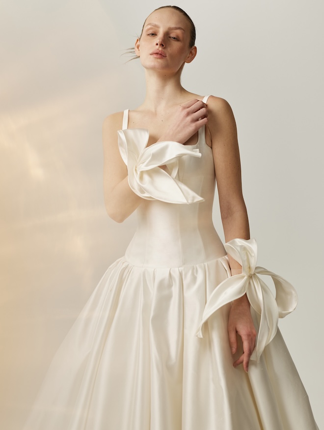The model wears an ivory drop waist wedding dress by Mira Zwillinger with floral wristbands. 