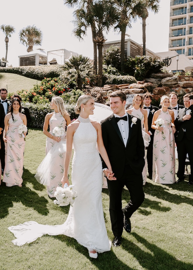 The couple and their wedding party walk on the lawn of a wedding venue in Galveston, The San Luis Resort, Spa and Conference Center.