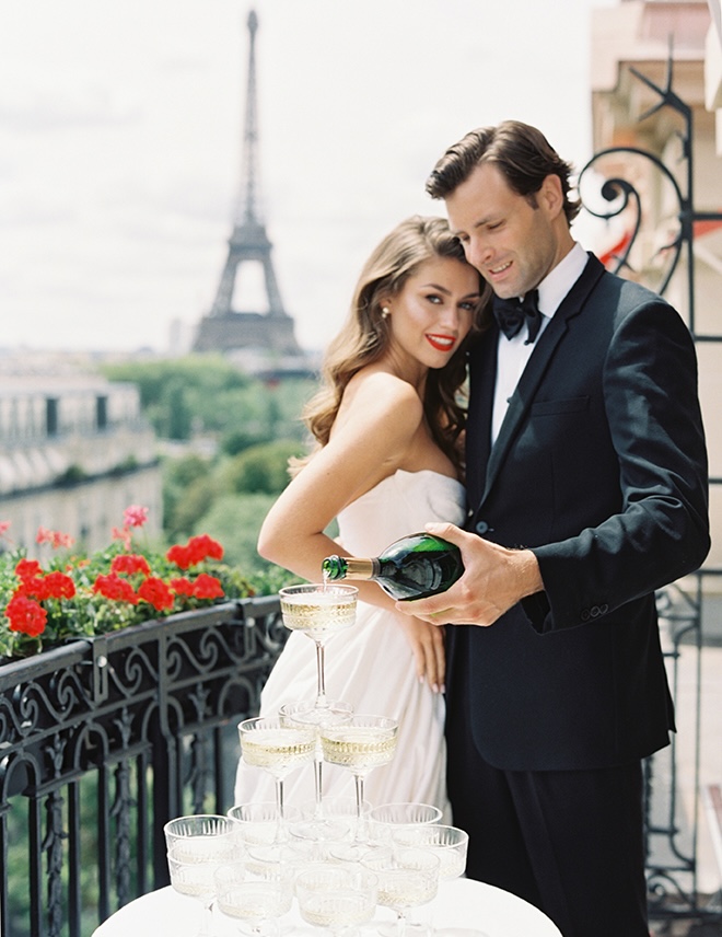 The couple pours Champagne into coupe glasses on the terrace.