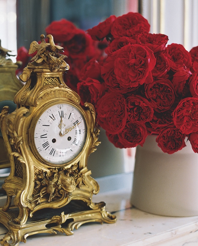 An antique clock sits next to a bouquet of red ranunculus on the fireplace in Paris wedding editorial. 