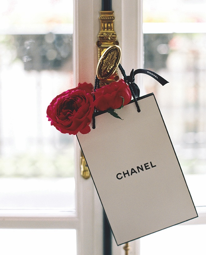 A Chanel shopping bag with a few stems of red ranunculus hangs off an antique doorknob of Paris wedding editorial.