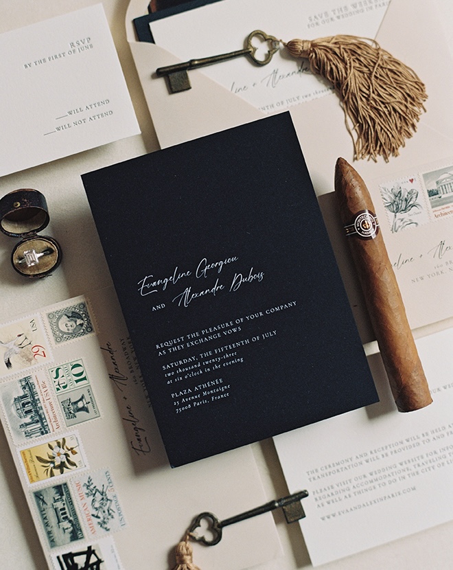 Black and white wedding stationery and invitations lay next to vintage keys and a cigar. 