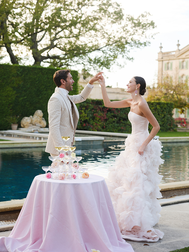 The couple holds hands next to a Champagne tower.