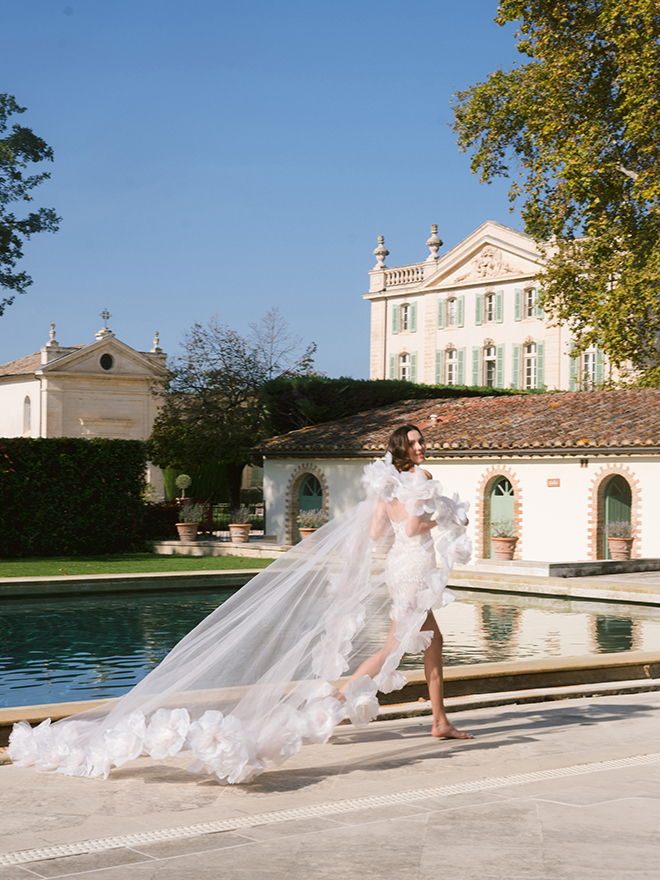 The bride runs next to the pool wearing a white mini dress and floral veil. 