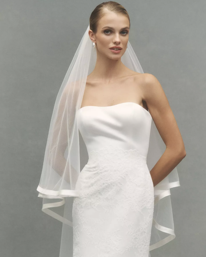 The model wears a satin trim chapel veil with blusher.