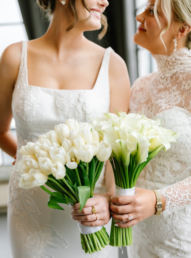The two brides hold long-stem wedding bouquets out of tulips and calla lilies. 