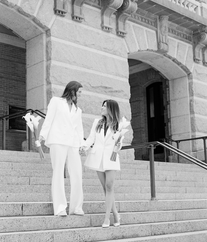 The two brides hold hands as they walk down the steps of a Houston courthouse. 