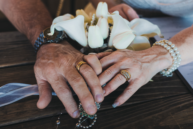 Close up of the newlyweds hands showing stunning gold rings with white flowers.