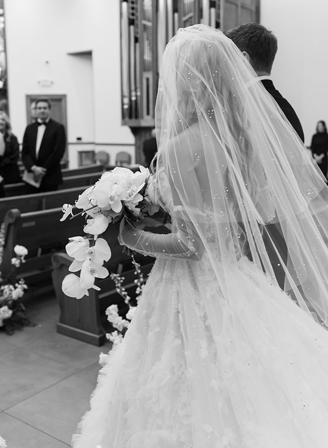 The bride walks down the aisle holding her wedding bouquet and wearing her wedding veil.