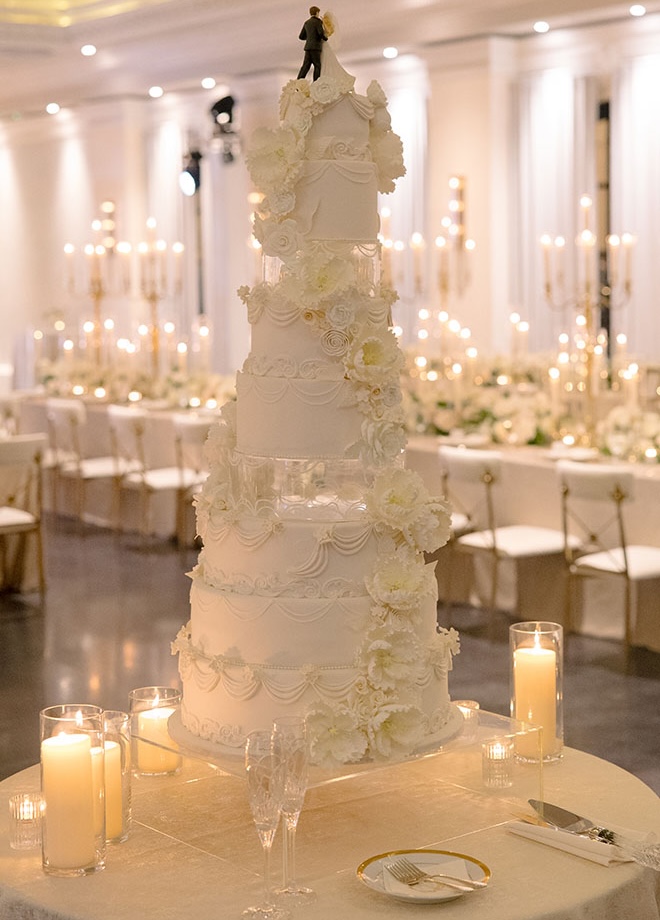 A nine-tier wedding cake embellished with flowers is the center of the reception with a bride and groom cake topper. 