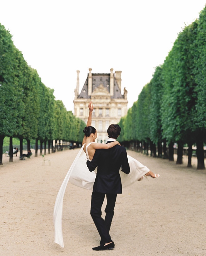 The groom spins the bride around in their Paris wedding photography in front of a French building. 