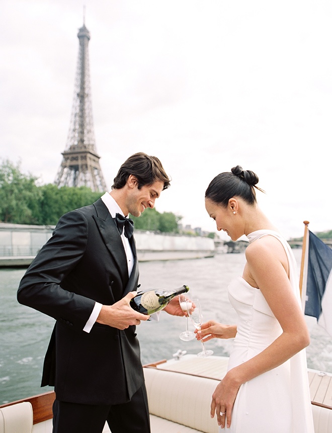 The groom pours a glass of Champagne for the bride on the boat. 