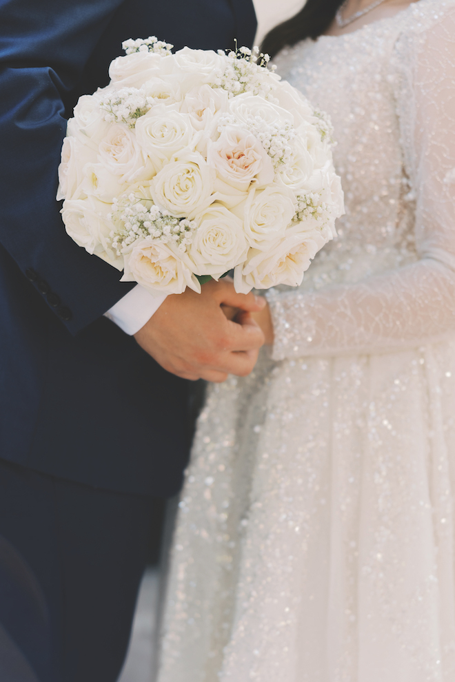 Close up of newlyweds holding the bridal baby breath's and rose bridal bouquet.