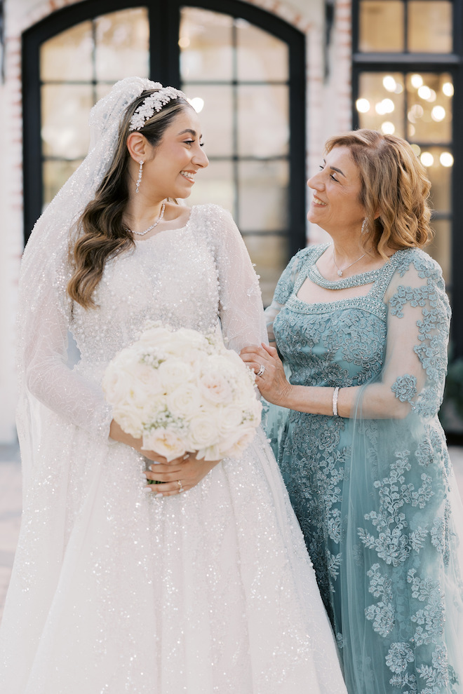 Mother of the bride in blue dress staring and smiling with the bride while the bride holds her baby breath's bouquet.