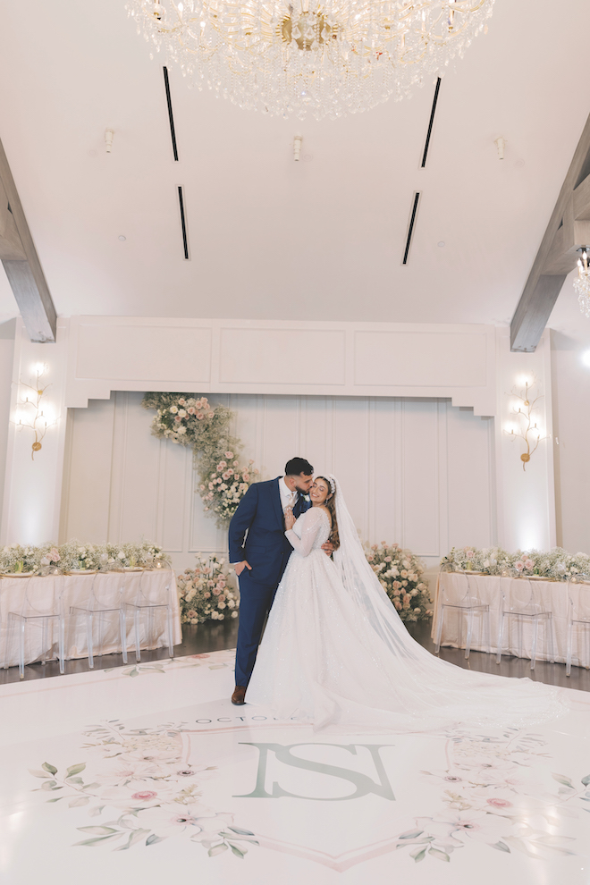 Groom kissing the bride on the cheek on the dance floor surrounded by florals.