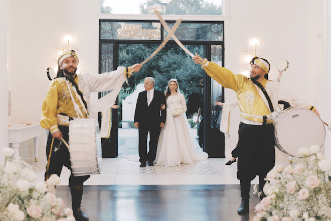 Father of the bride and bride walking in to venue down the aisle with traditional middle eastern sword entrance.