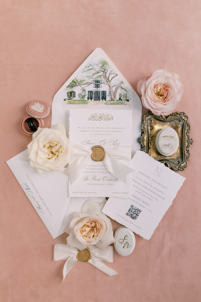 White invitations on light pink backdrop with white and pink roses around with rings and minor details.