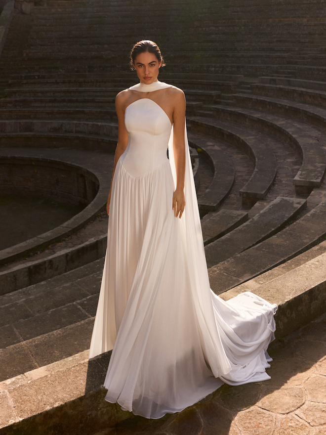 Elegant white flowy wedding gown with bridal scarf in pretty lighting.