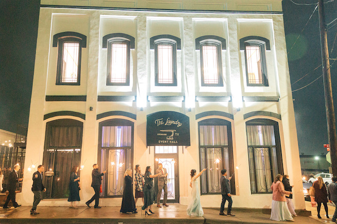 Outside of hill country wedding venue that's white with black details with guests cheering outside.