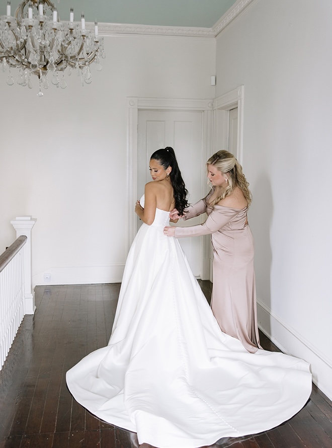 A bridesmaid helps the bride into her wedding dress. 