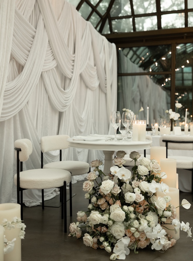 White drapery and ivory colored florals decorate the glass atrium wedding venue. 