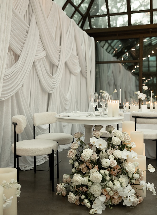 White drapery and ivory florals decorate the glass atrium wedding venue.