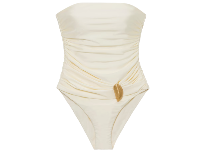 A one-piece ivory colored strapless swimsuit with a seashell pendant. 