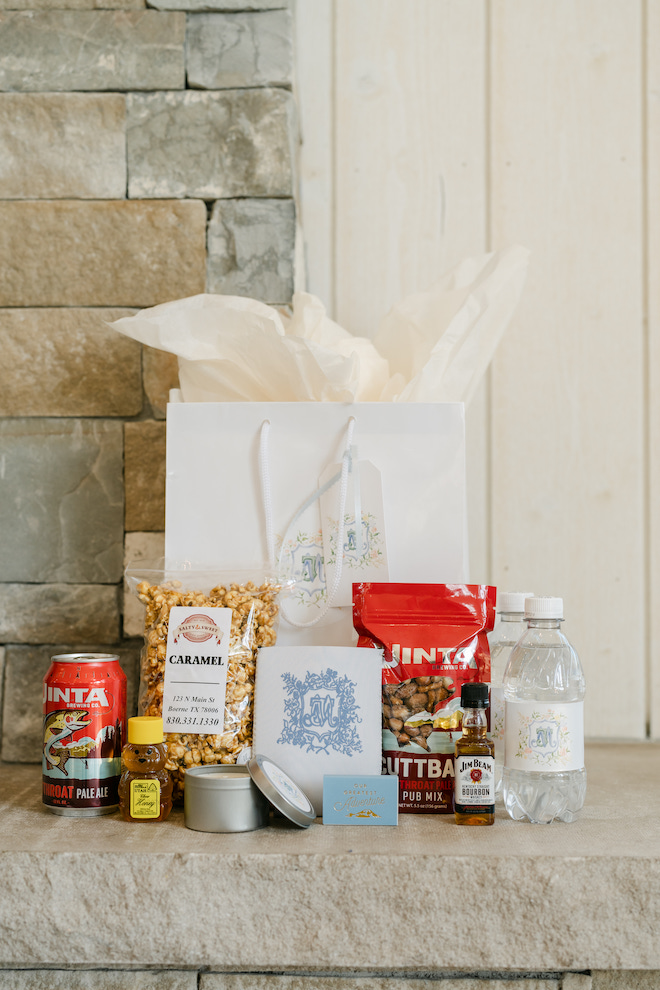 White gift bag surrounded by goodies to go inside in front of stone wall.
