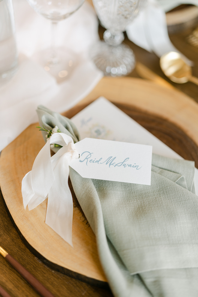 Sage green linen napkin with place card tied to it with the guests' name on it.